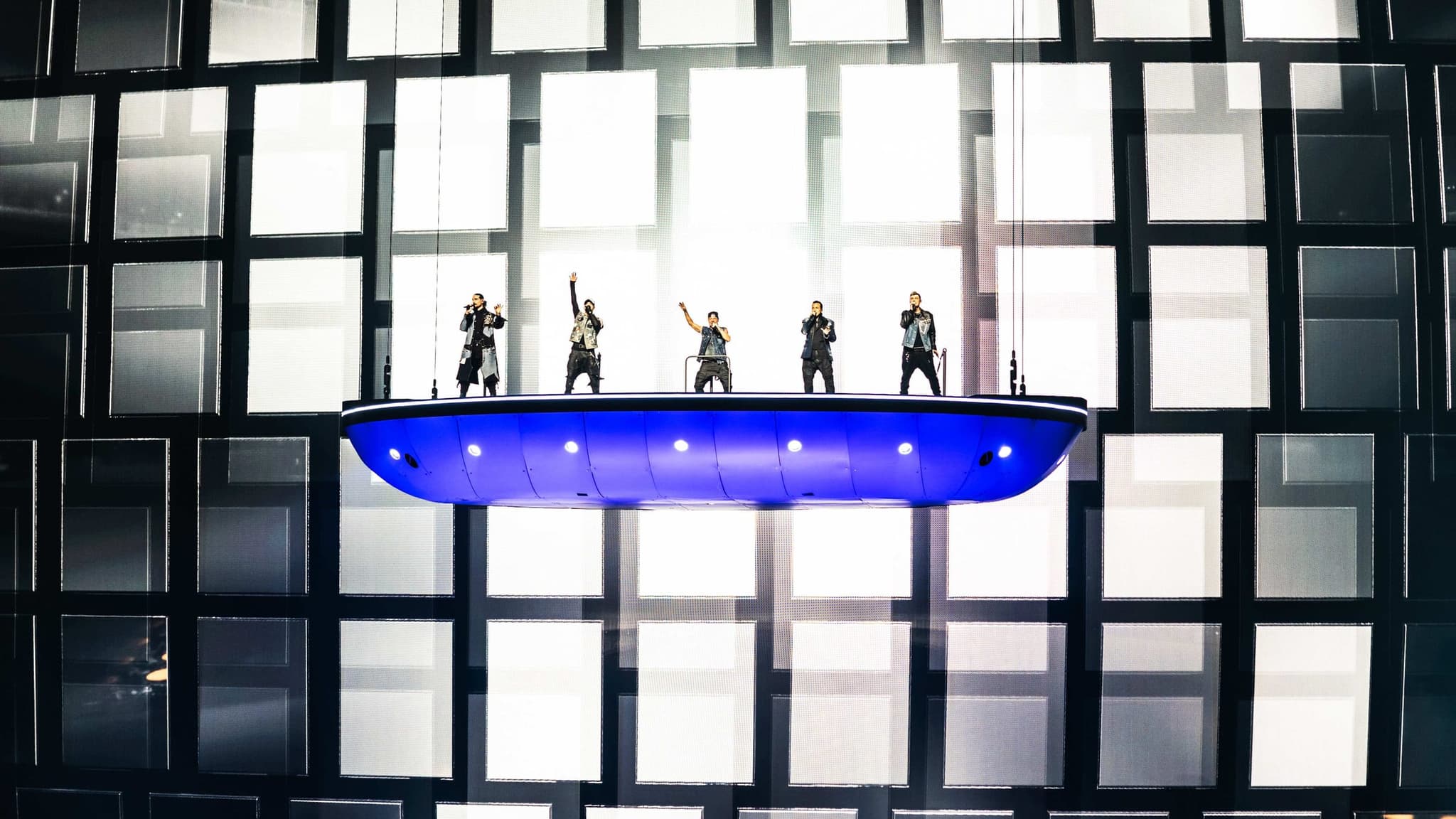 The five Backstreet Boys performing on a flying blue stage platform in front of a lit grid of screens at Sphere, Las Vegas.